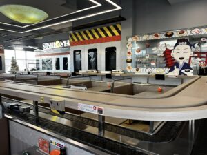 Modern sushi restaurant interior with conveyor belt system, cartoon chef mural, and Japanese-themed decor