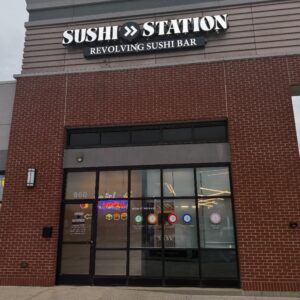 Sushi Station revolving sushi bar restaurant storefront with brick exterior, large windows, and colorful signage at locati...