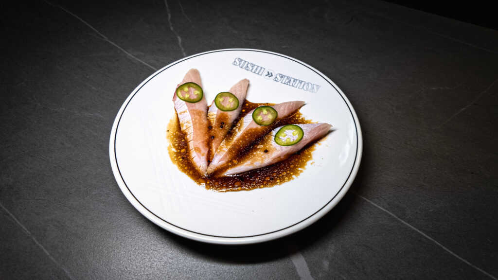 Sliced sashimi with jalapeño and ponzu sauce artfully plated on white ceramic dish at restaurant