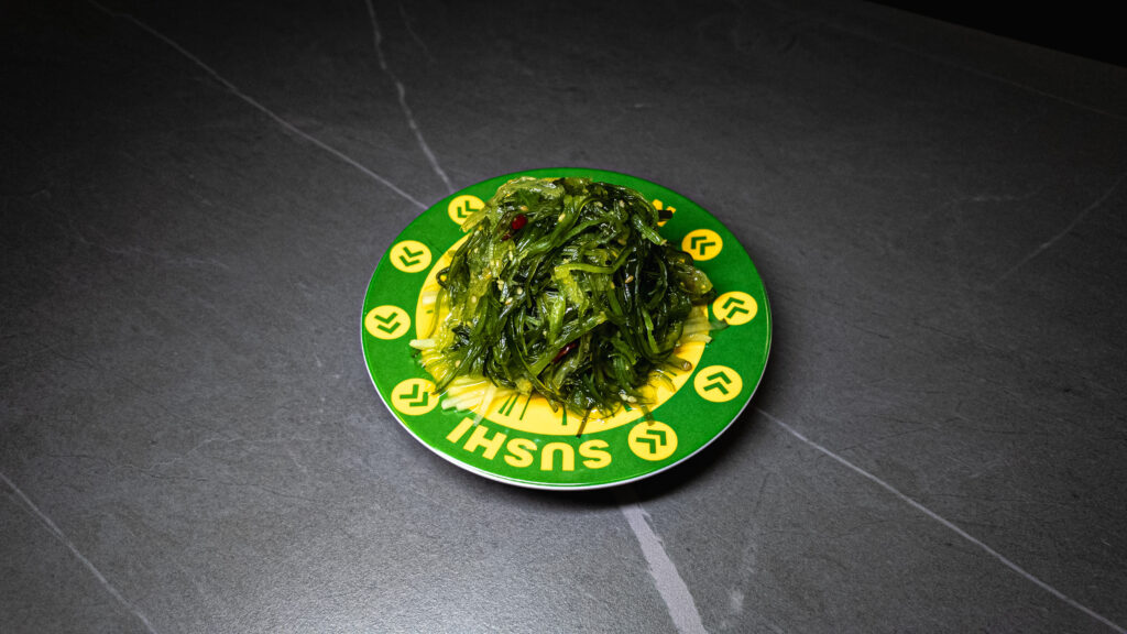 Seaweed salad served on green branded plate at Crowdfavorites restaurant on dark tile surface