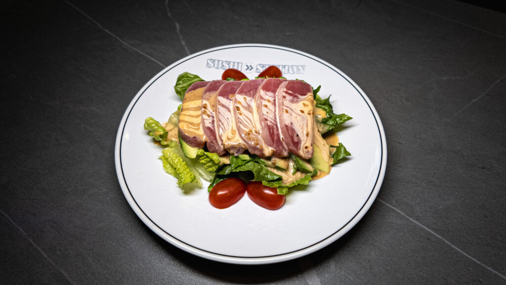 Seared tuna salad with mixed greens, avocado and cherry tomatoes served on white plate at restaurant