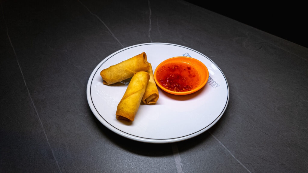 Three golden spring rolls with sweet and sour dipping sauce served on white plate at restaurant