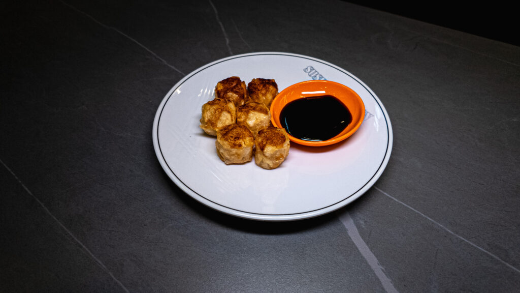 Golden fried dumplings served on white plate with soy sauce dipping bowl at restaurant