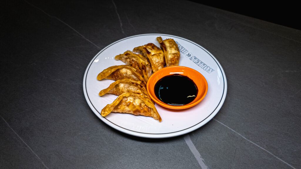 Golden pan-fried dumplings arranged on white plate with soy sauce dipping bowl at restaurant
