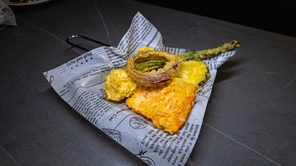 Tempura vegetables including battered squash blossom and root vegetables served on newspaper at restaurant