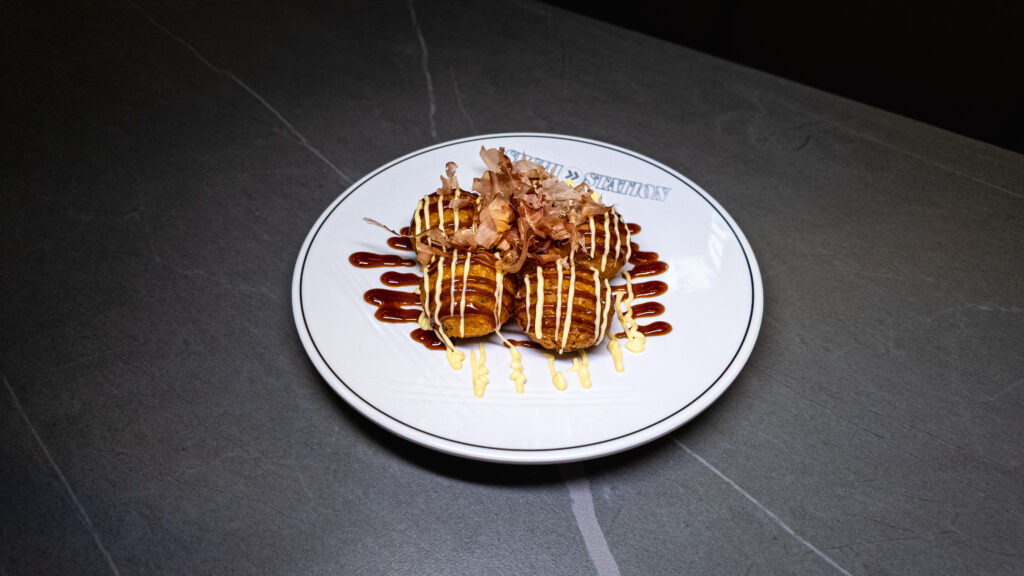 Gourmet takoyaki balls drizzled with mayo and teriyaki sauce, topped with bonito flakes on white restaurant plate