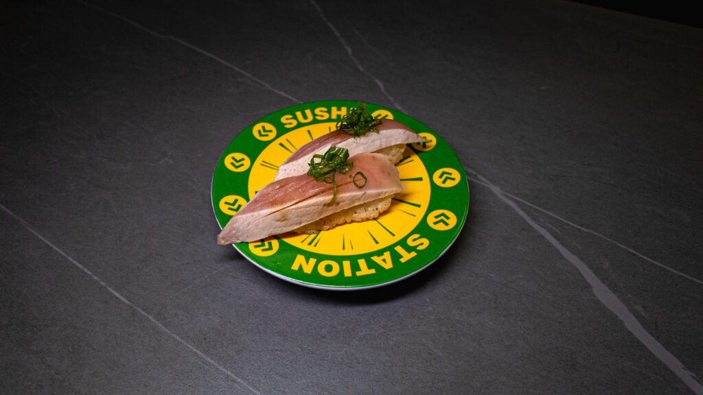 Fresh sushi nigiri with raw fish and herbs served on green Sushi Station conveyor belt plate at restaurant