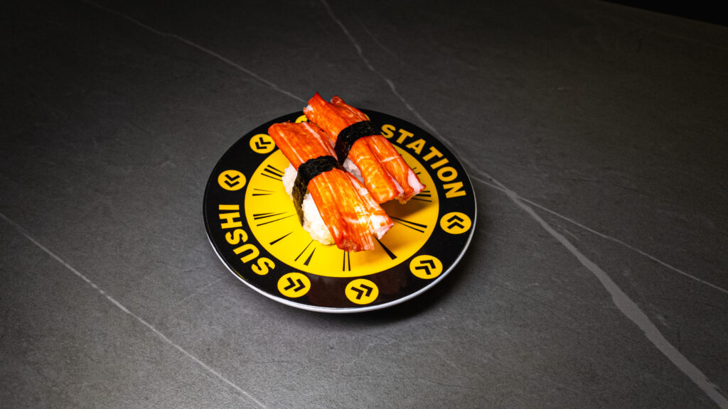 Fresh salmon sushi nigiri served on black plate with yellow clock design at restaurant on dark tiled surface