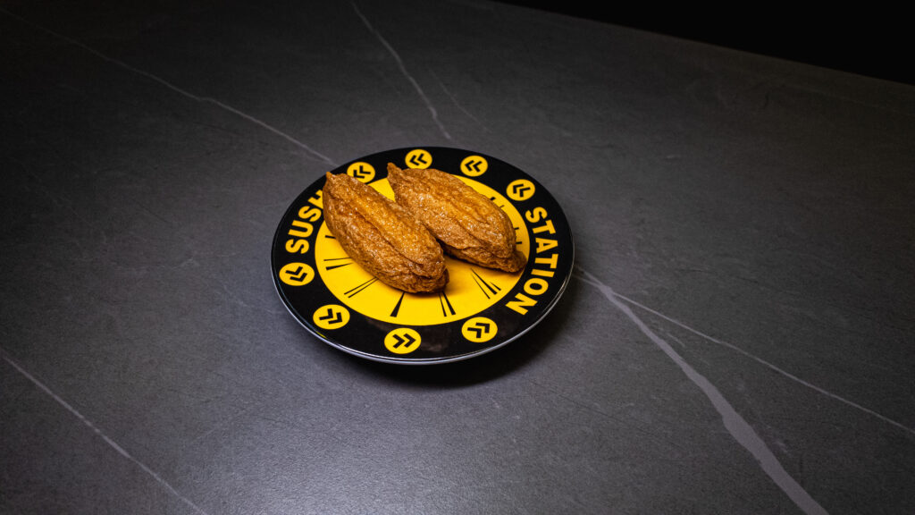 Two golden-brown eclairs on black and yellow branded plate at CROWDFAVORITES restaurant on dark tiled surface