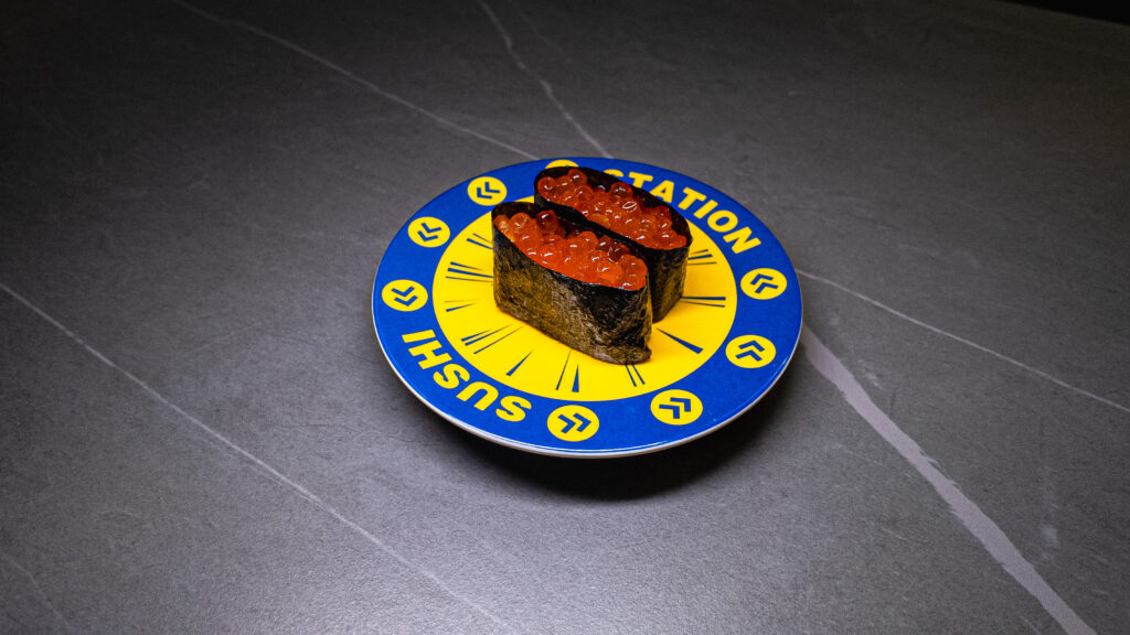 Two pieces of ikura salmon roe sushi on yellow conveyor belt sushi restaurant plate with clock design