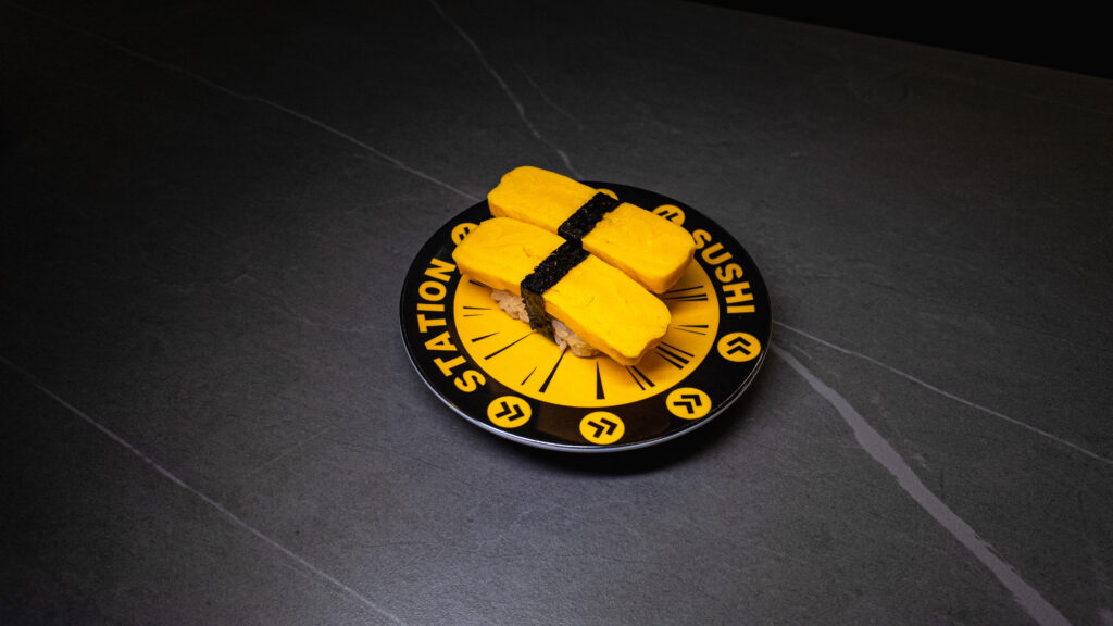 Fresh tamago sushi on branded yellow and black station plate on dark tiled restaurant table