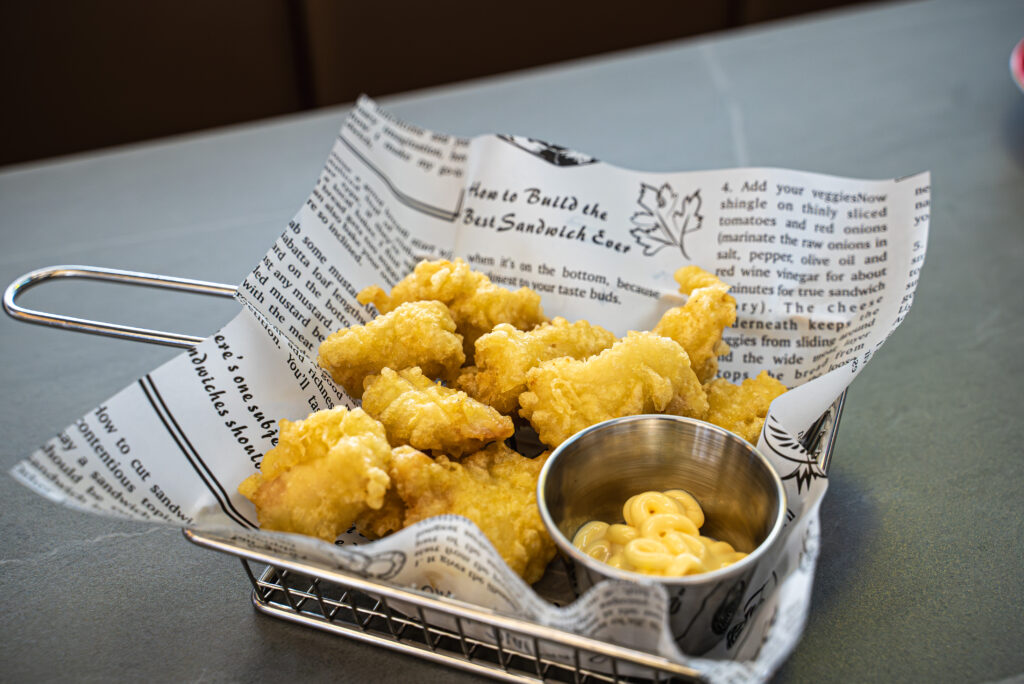 Golden fried cauliflower served in wire basket with newspaper liner and small bowl of yellow dipping sauce on restaurant t...