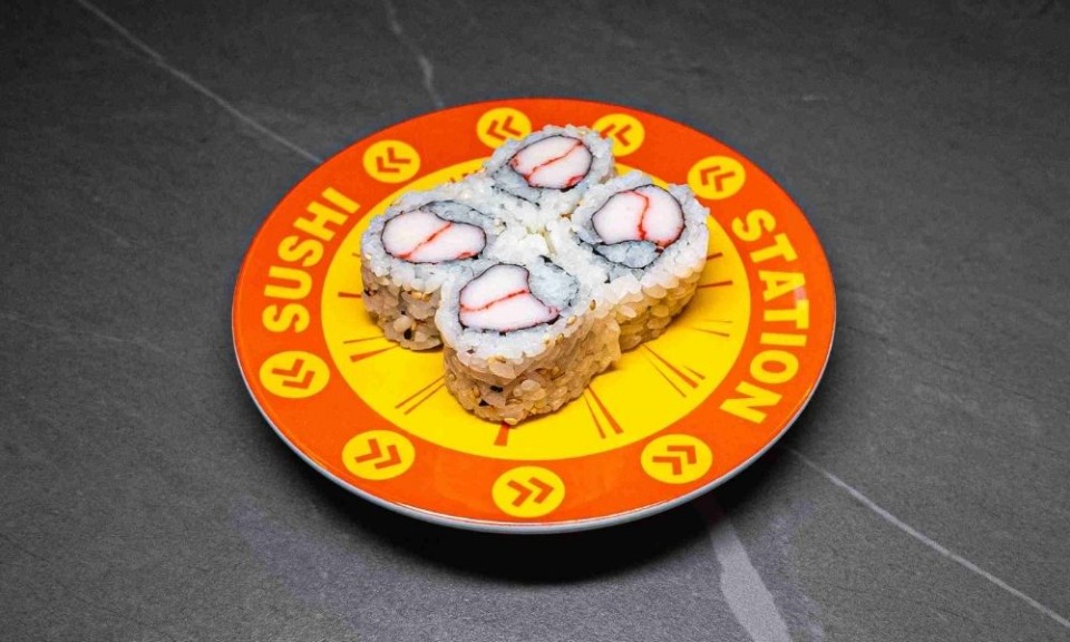 Sushi Station plate with four crab roll pieces, vibrant orange and yellow design, perfect for restaurant menu or food blog.