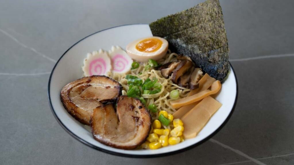 Ramen bowl with chashu pork, soft-boiled egg, nori, corn, green onions, and narutomaki at CROWDFAVORITES restaurant