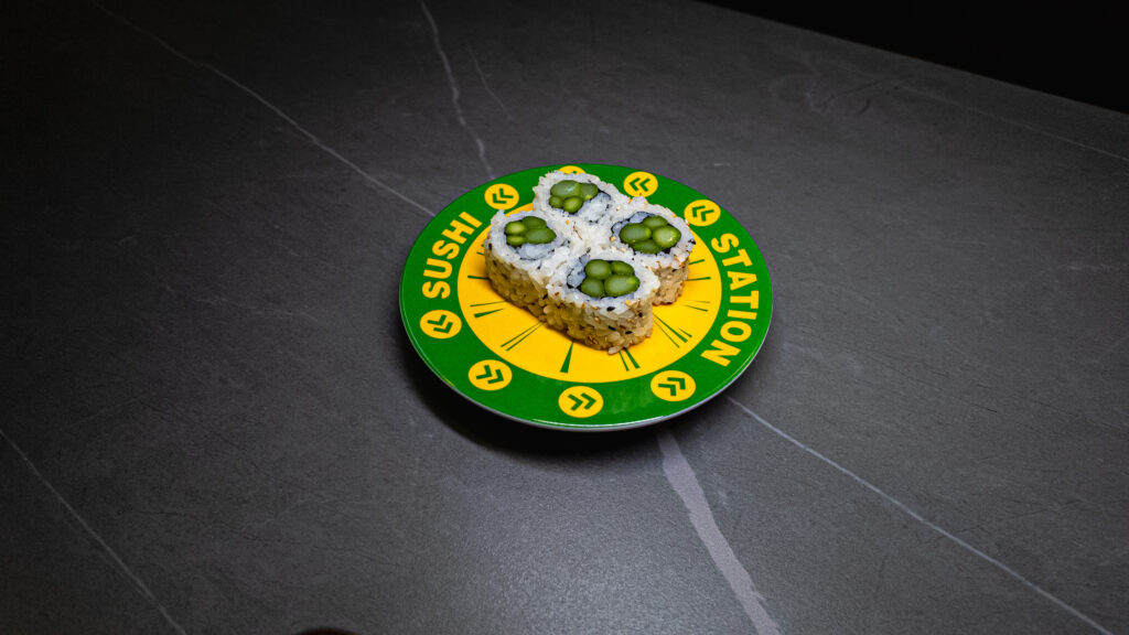 Sushi Station plate with four green-topped sushi rolls on dark table, perfect for restaurant menu or food blog SEO.