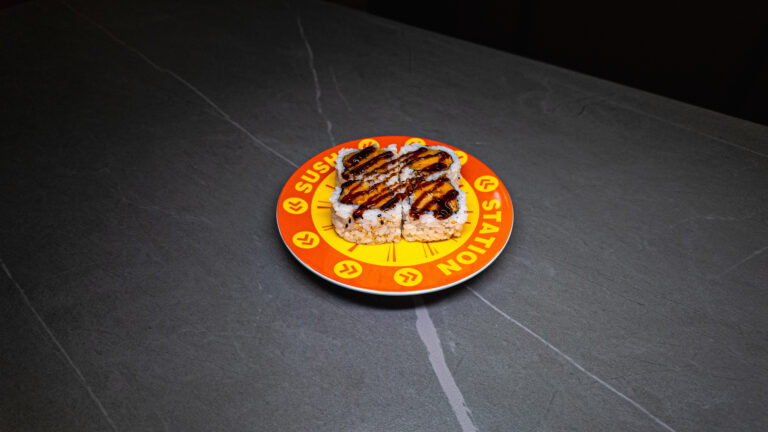 Sushi rolls with eel sauce on a vibrant orange "Sushi Station" plate, served at CROWDFAVORITES restaurant.