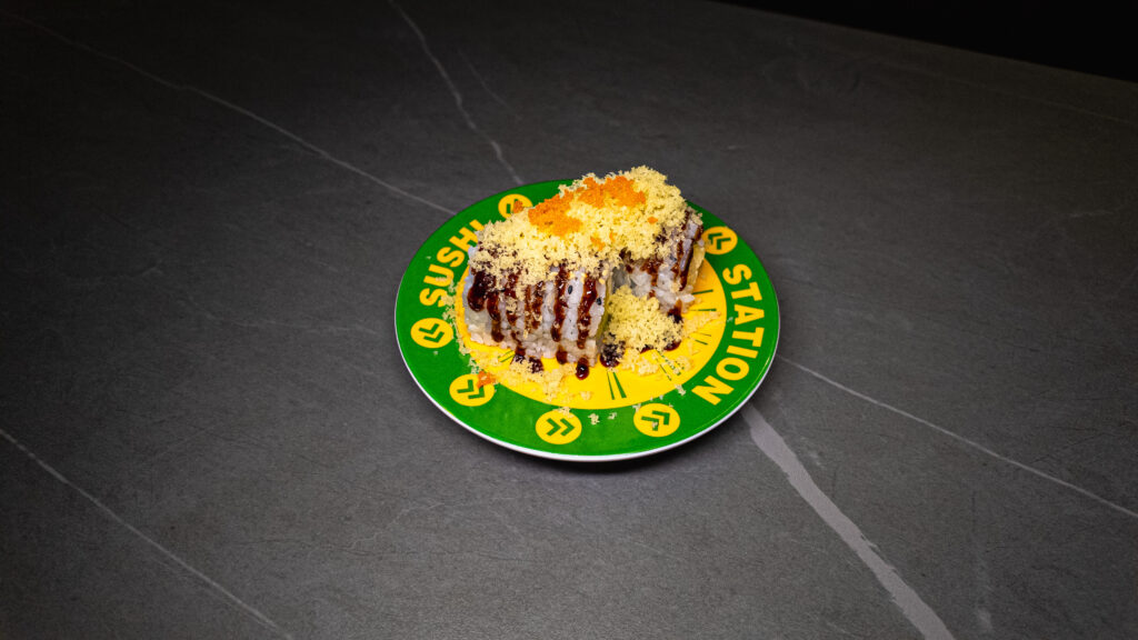 Gourmet sushi roll with tempura coating and sauce drizzle served on green Sushi Station branded plate