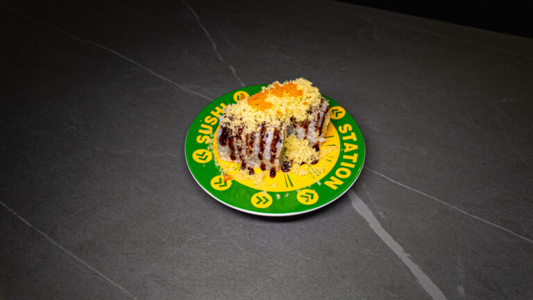 Gourmet sushi roll with tempura coating and sauce drizzle served on green Sushi Station branded plate