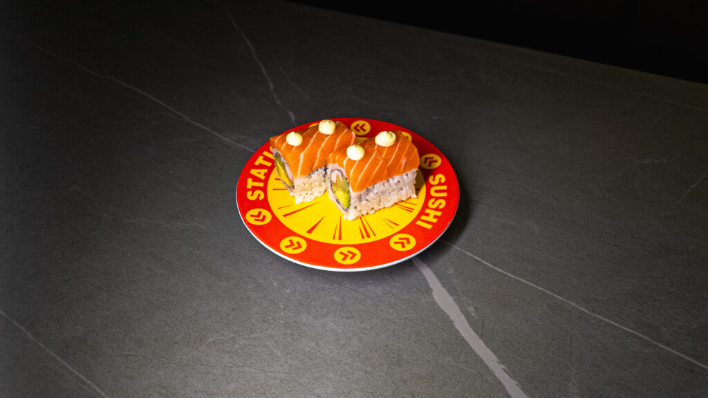 Fresh salmon sushi rolls with white sauce on branded restaurant plate against dark slate surface