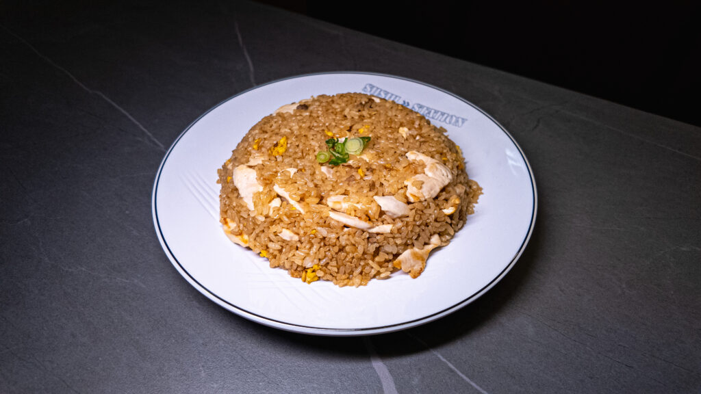 Chicken fried rice garnished with green onions, served on a white plate at CROWDFAVORITES restaurant.