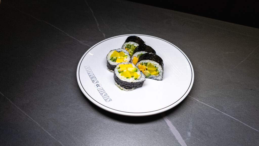 Fresh sushi rolls with mango, cucumber, and avocado on a white plate at CROWDFAVORITES restaurant.