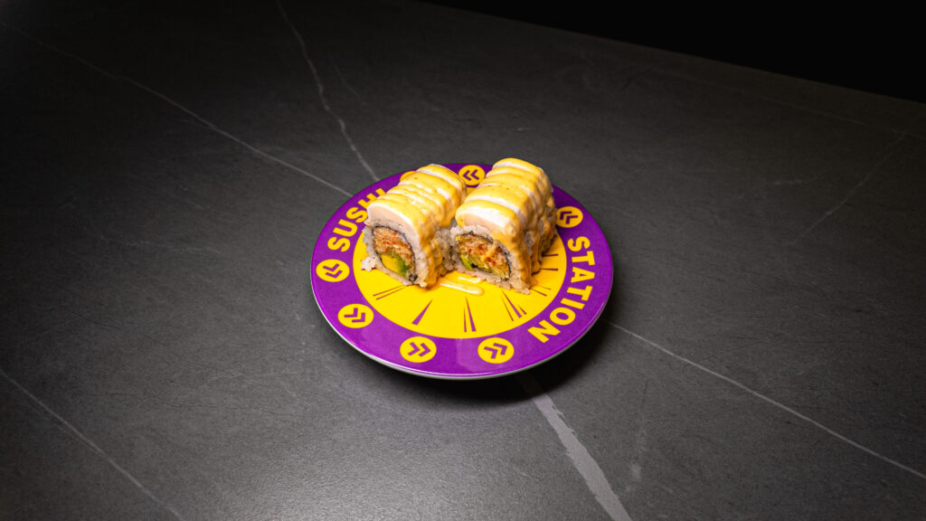 Sushi Station plate with two sushi rolls topped with yellow sauce, served on dark table for CROWDFAVORITES restaurant menu.