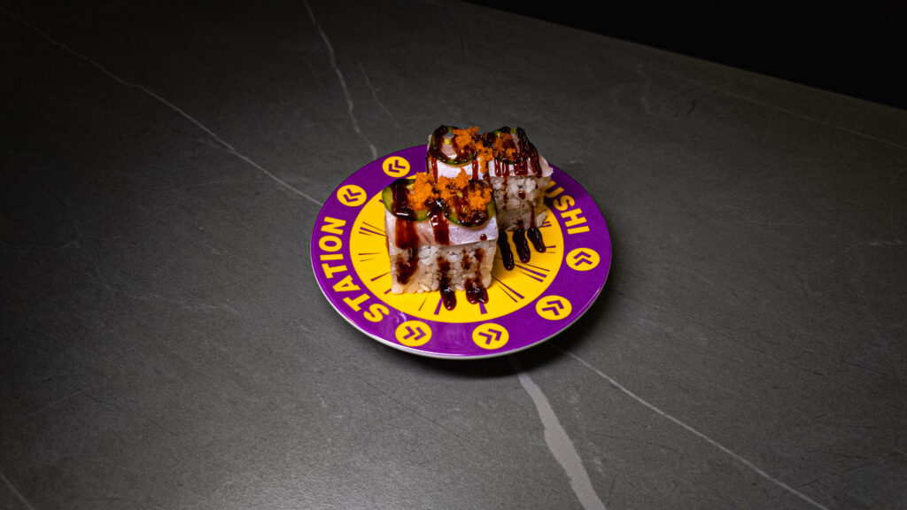 Sushi rolls with tobiko and sauce on purple "Sushi Station" plate, served at CROWDFAVORITES restaurant.
