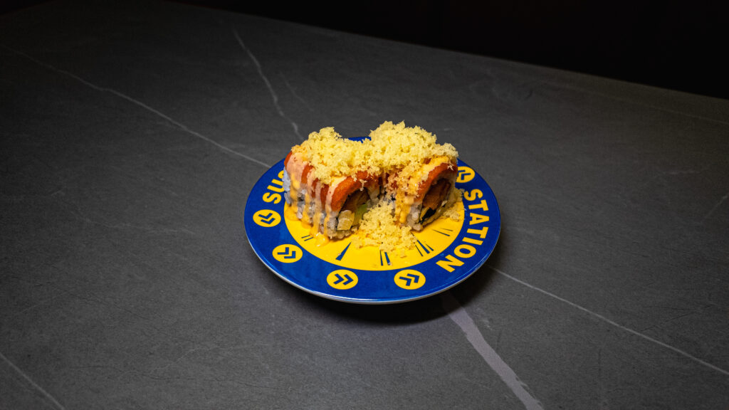 Crispy topped sushi roll on blue and yellow "Sushi Station" plate, served at CROWDFAVORITES restaurant.