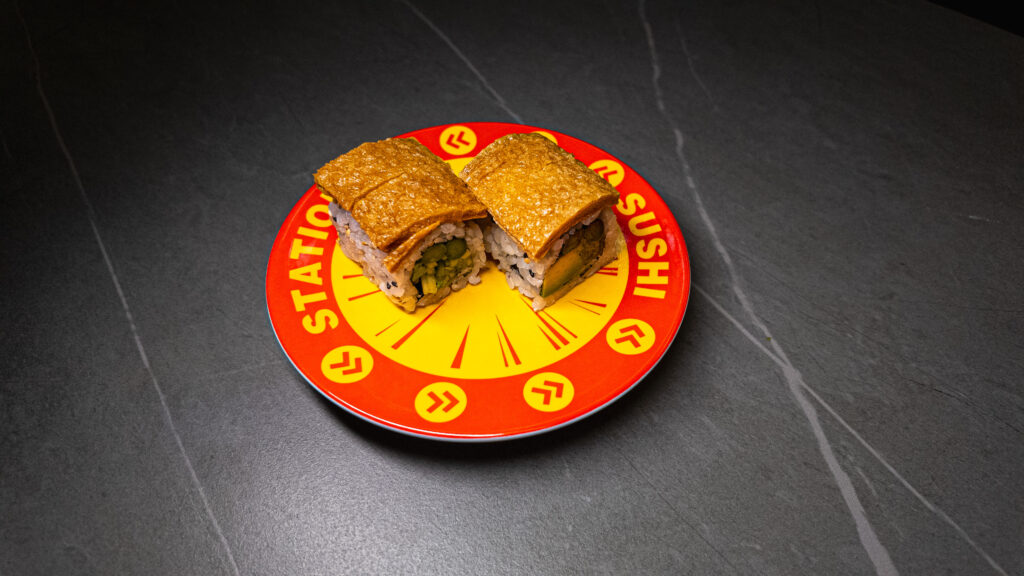 Two sushi rolls with crispy topping on red "Station Sushi" plate, served at CROWDFAVORITES restaurant.