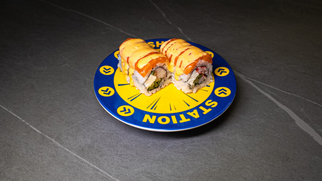 Sushi rolls with cheese sauce on blue and yellow "STATION" plate at CROWDFAVORITES restaurant