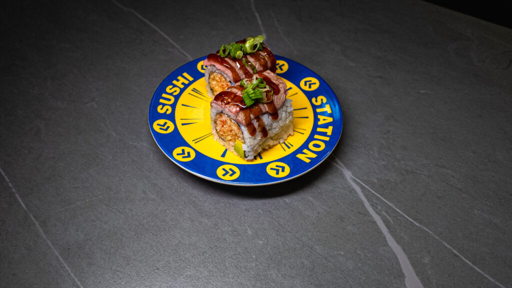 Sushi Station plate with gourmet sushi rolls topped with sauce and green onions, served at CROWDFAVORITES restaurant