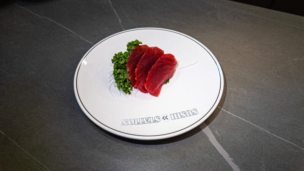 Fresh tuna sashimi with green garnish on white plate at CROWDFAVORITES restaurant, elegantly presented for sushi lovers.