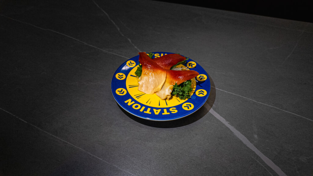 Sushi Station plate with vibrant orange uni on green garnish, served at CROWDFAVORITES restaurant for seafood lovers.