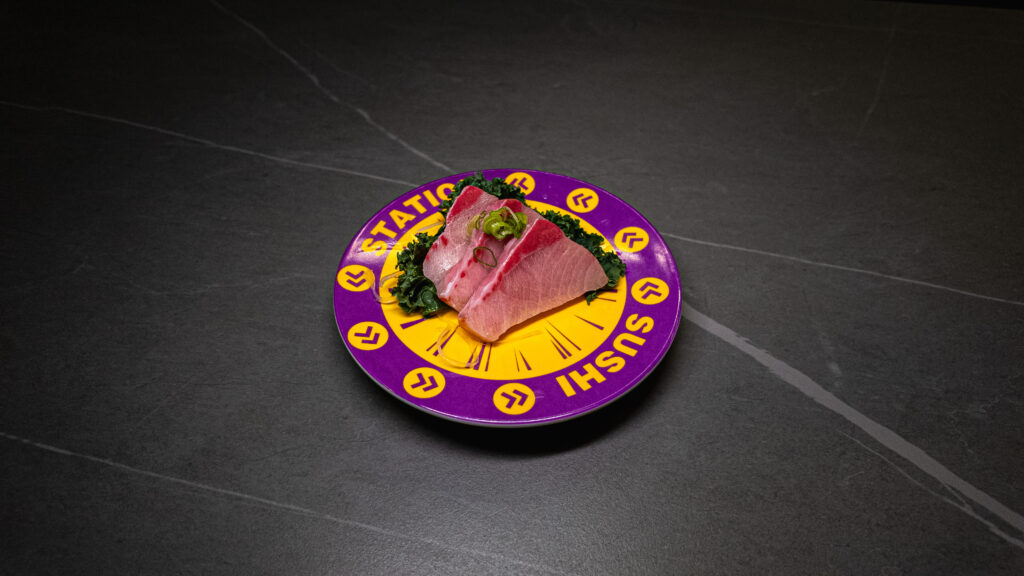 Fresh tuna sashimi on purple and yellow Station Sushi plate, garnished with greens, served at CROWDFAVORITES restaurant.