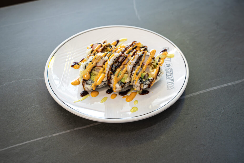 Sushi rolls with eel sauce and spicy mayo on a white plate at CROWDFAVORITES restaurant, perfect for sushi lovers.