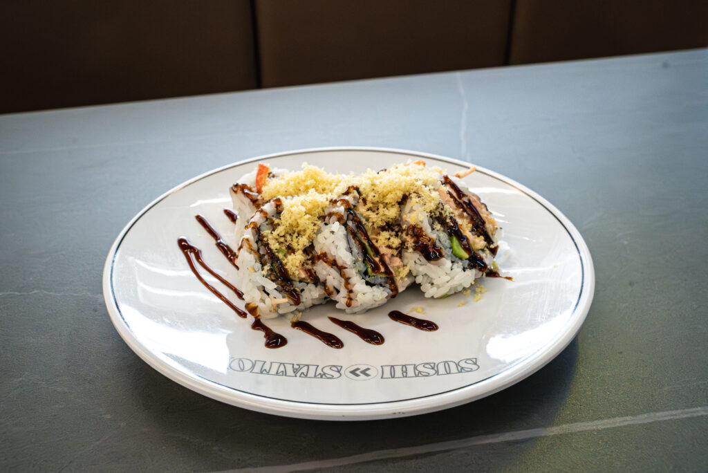 Sushi roll with crispy topping and sauce drizzle on white plate at CROWDFAVORITES restaurant