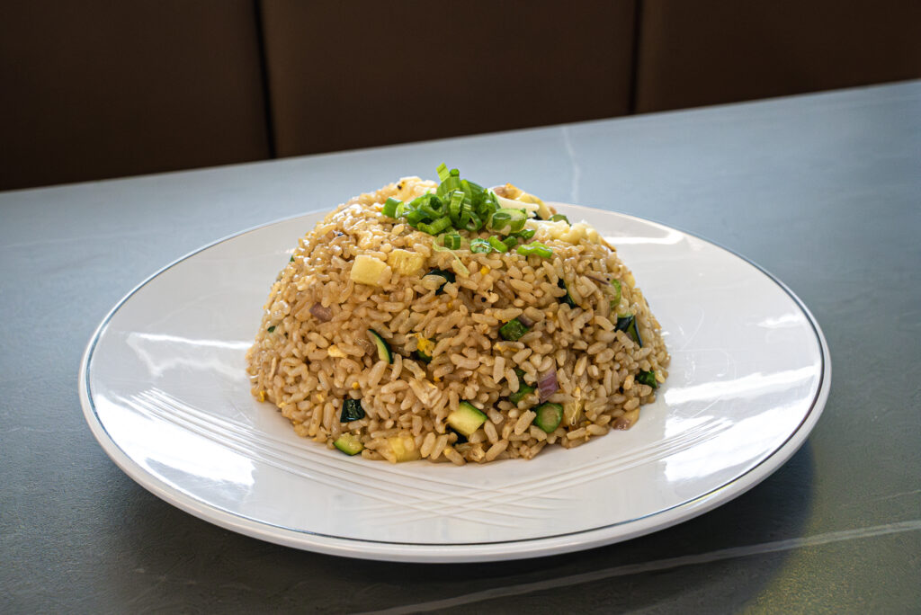 Fried rice with vegetables and green onions, served at CROWDFAVORITES restaurant on a white plate.