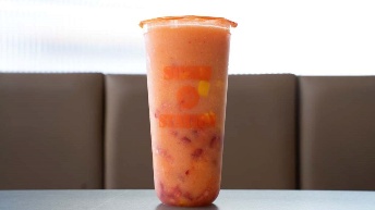 Fresh orange smoothie in branded cup at CROWDFAVORITES restaurant, served on table with booth seating background