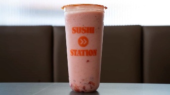 Pink strawberry smoothie in Sushi Station cup, served at CROWDFAVORITES restaurant with brown booth background