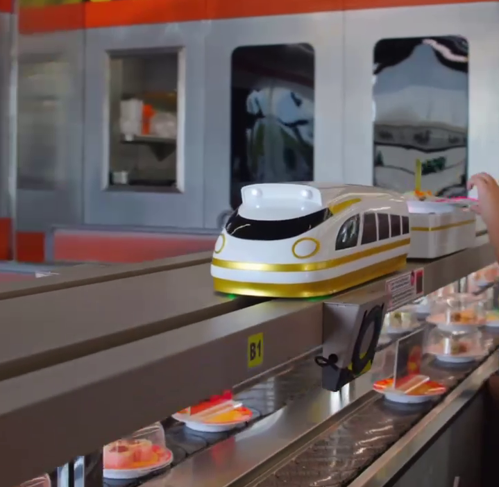 Automated conveyor belt sushi restaurant with train-shaped delivery system carrying plates of food to customers